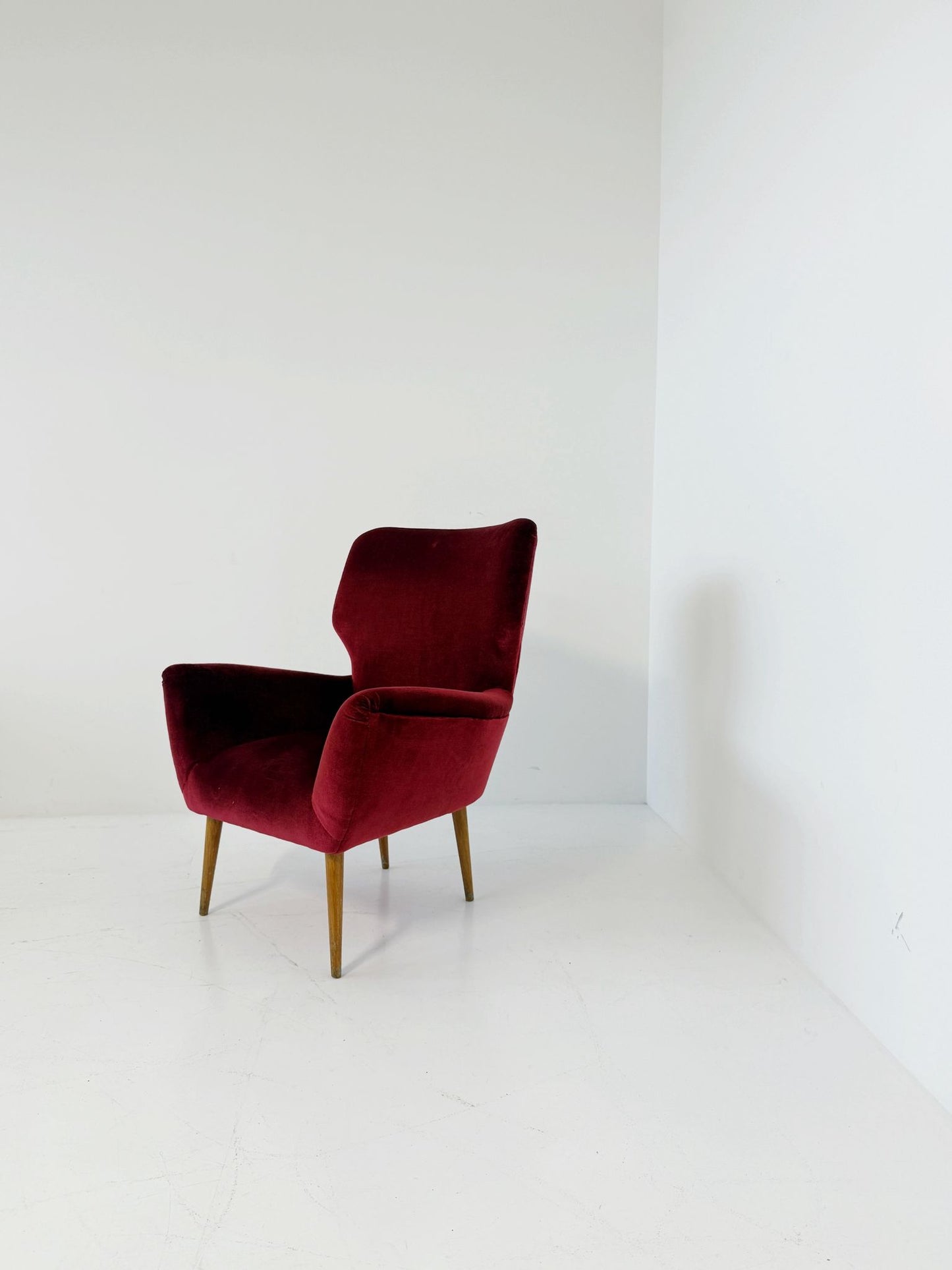 An elegant 1950s-style armchair upholstered in burgundy velve