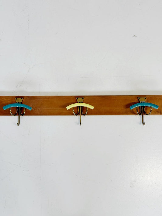 Wooden wall-mounted coat rack with three curved brass hooks and colored Bakelite