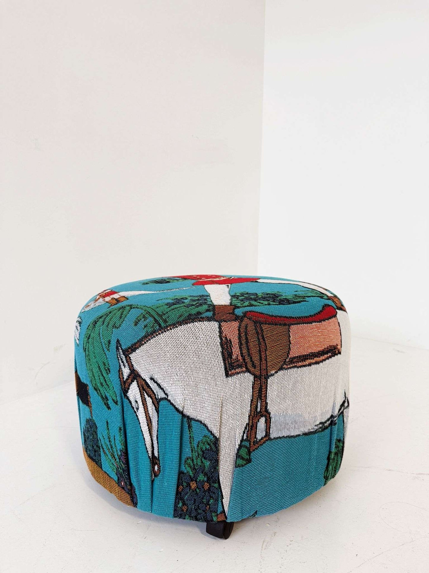 A cylindrical pouf covered in turquoise jacquard fabric, decorated with a naive-inspired figurative motif