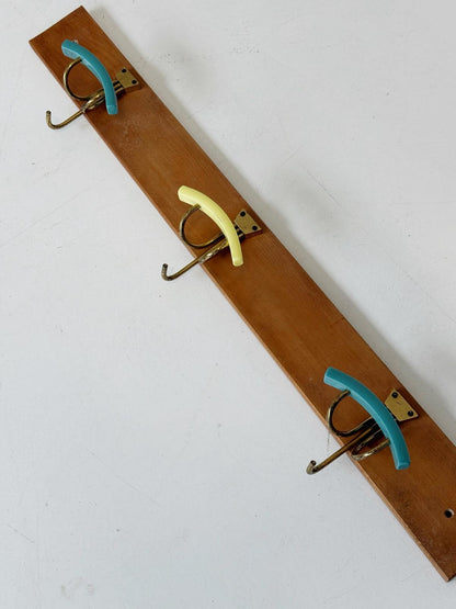 Wooden wall-mounted coat rack with three curved brass hooks and colored Bakelite
