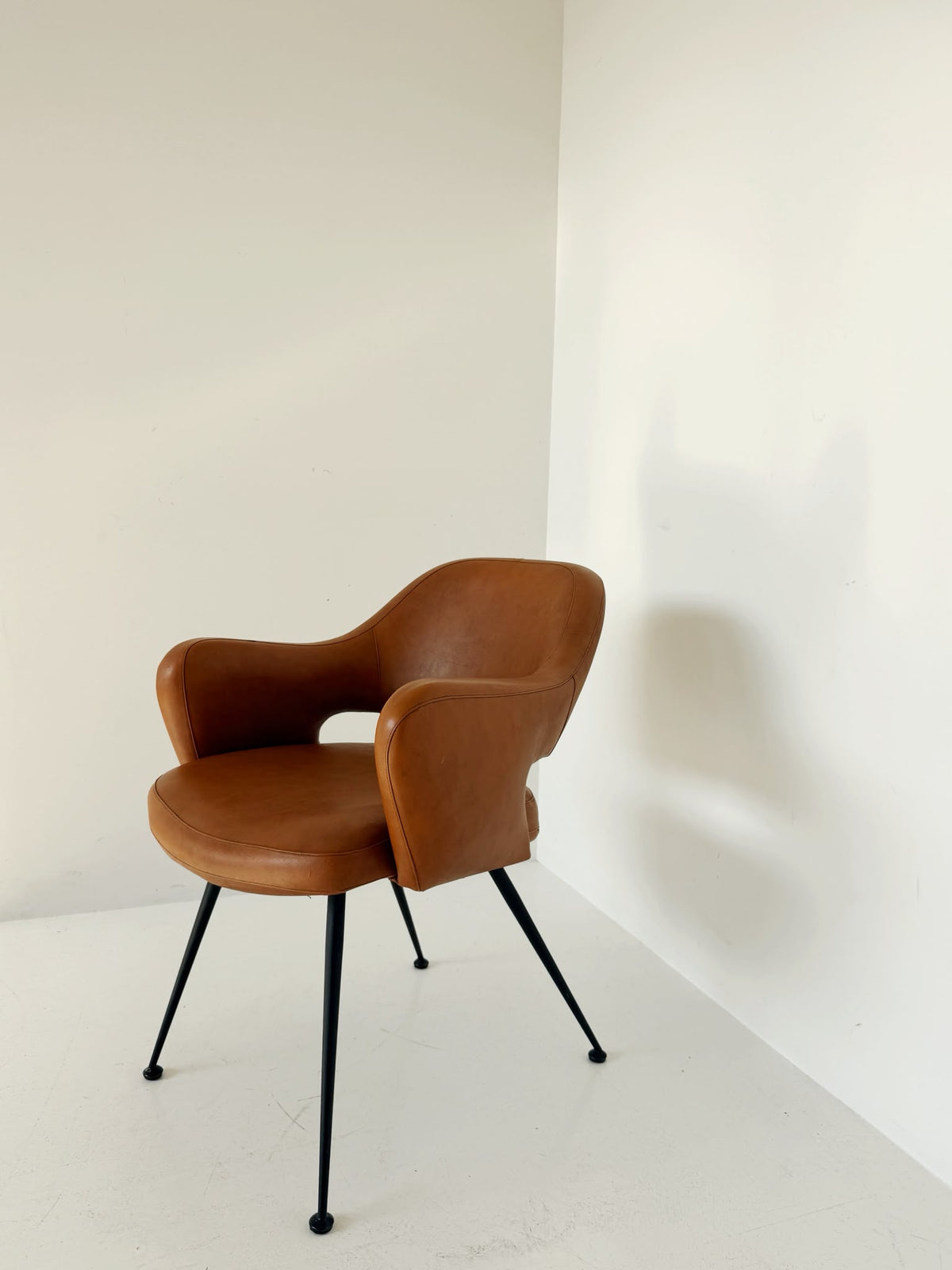 Poltroncina imbottita in pelle color cognac con struttura in metallo nero, anni ’50/’60.