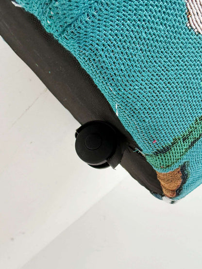 A cylindrical pouf covered in turquoise jacquard fabric, decorated with a naive-inspired figurative motif
