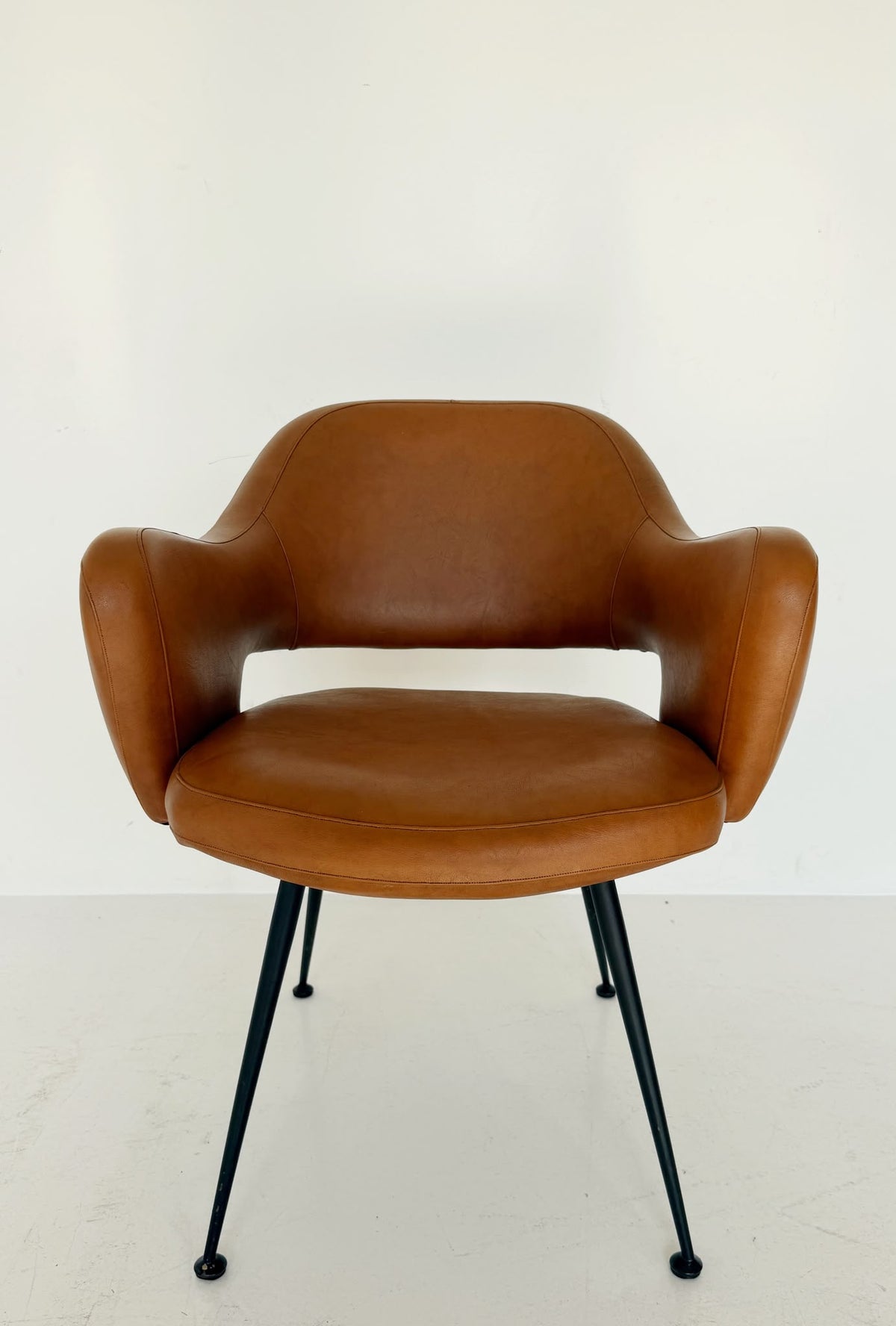 Poltroncina imbottita in pelle color cognac con struttura in metallo nero, anni ’50/’60.