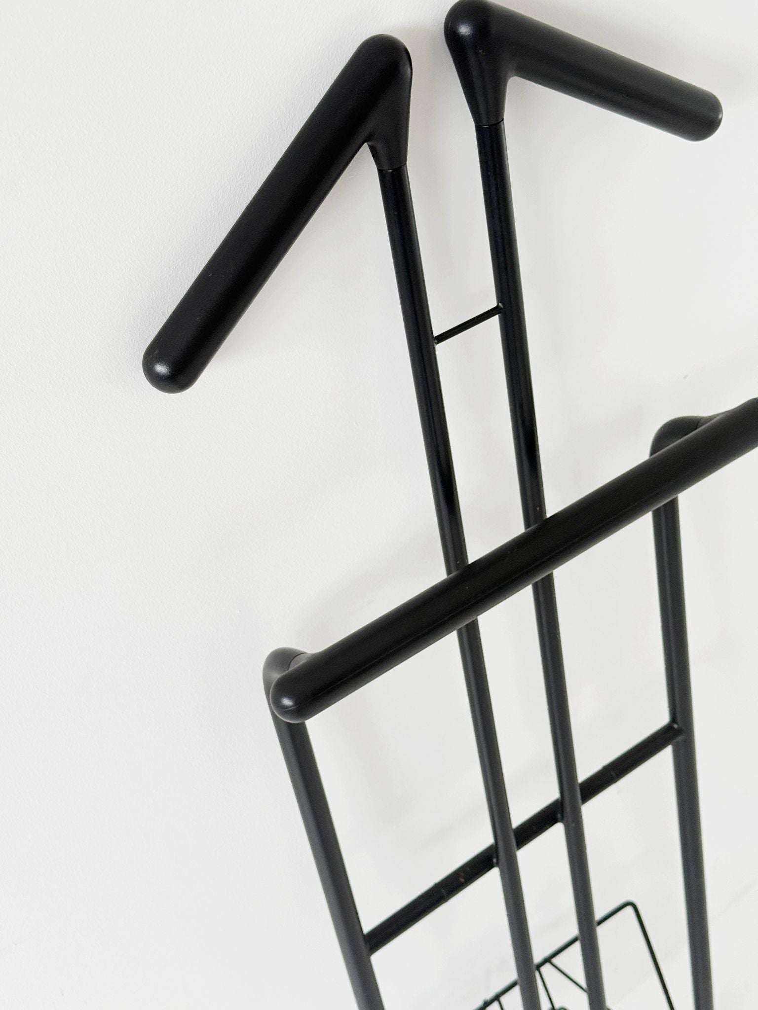 Folding coat rack made of black painted tubular metal, with a cross-strut structure.
