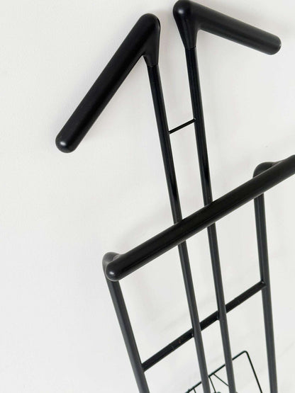 Folding coat rack made of black painted tubular metal, with a cross-strut structure.