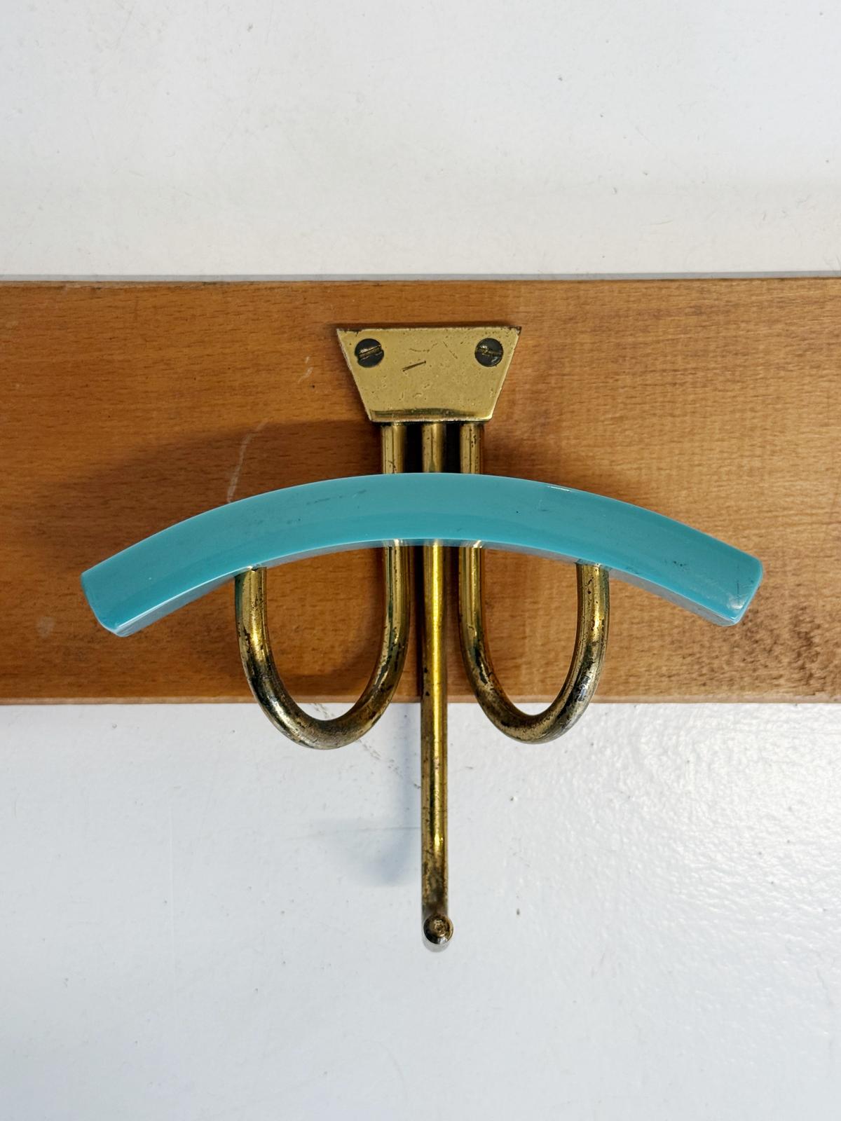 Wooden wall-mounted coat rack with three curved brass hooks and colored Bakelite