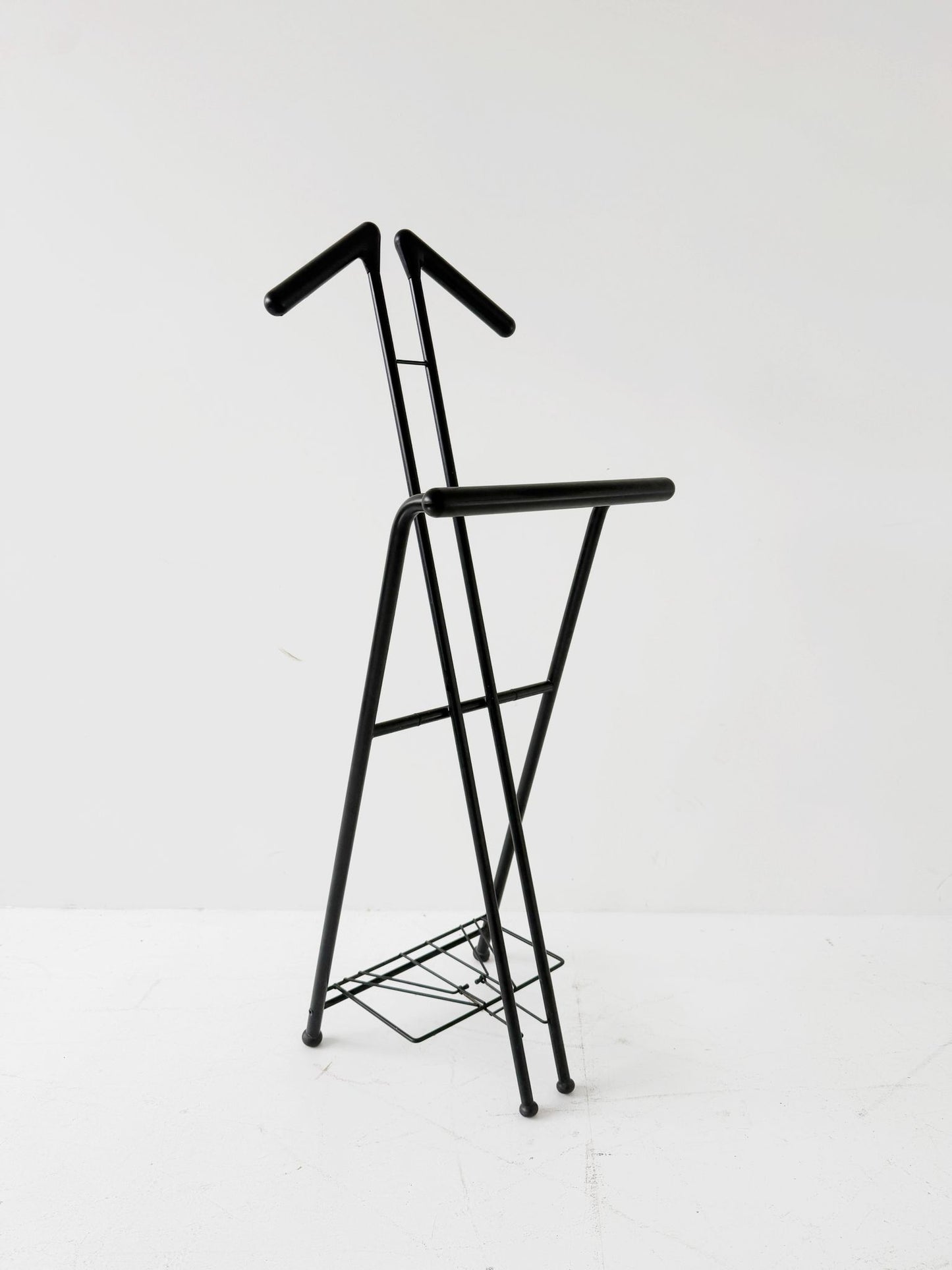 Appendiabiti da terra pieghevole in tubolare metallico verniciato nero, con struttura a montanti incrociati.
