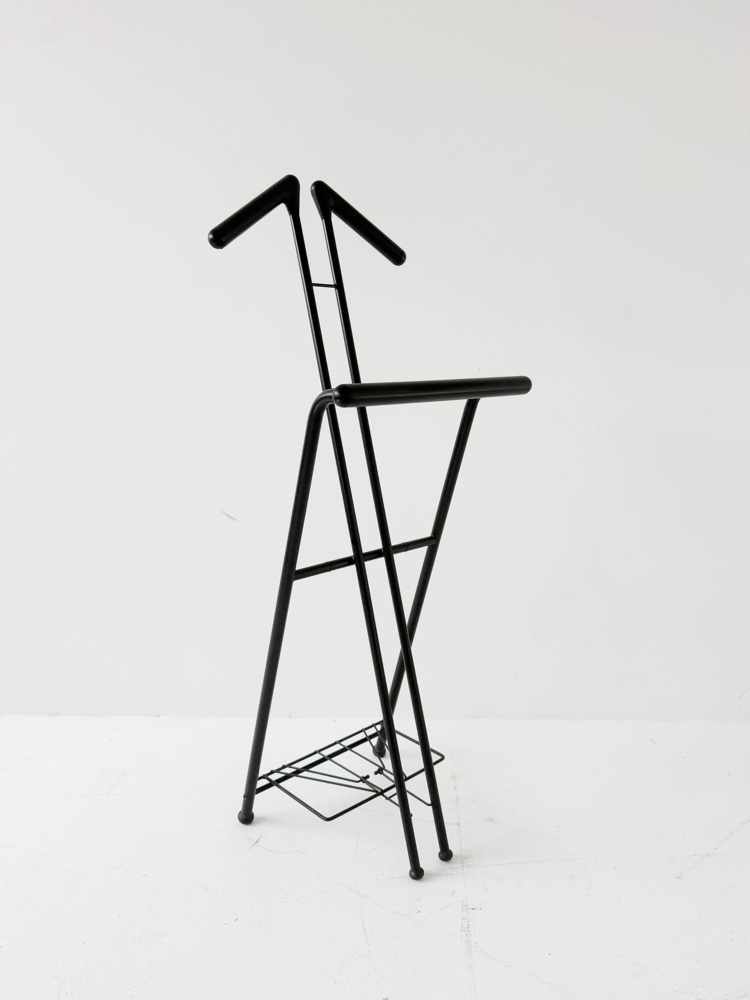 Appendiabiti da terra pieghevole in tubolare metallico verniciato nero, con struttura a montanti incrociati.
